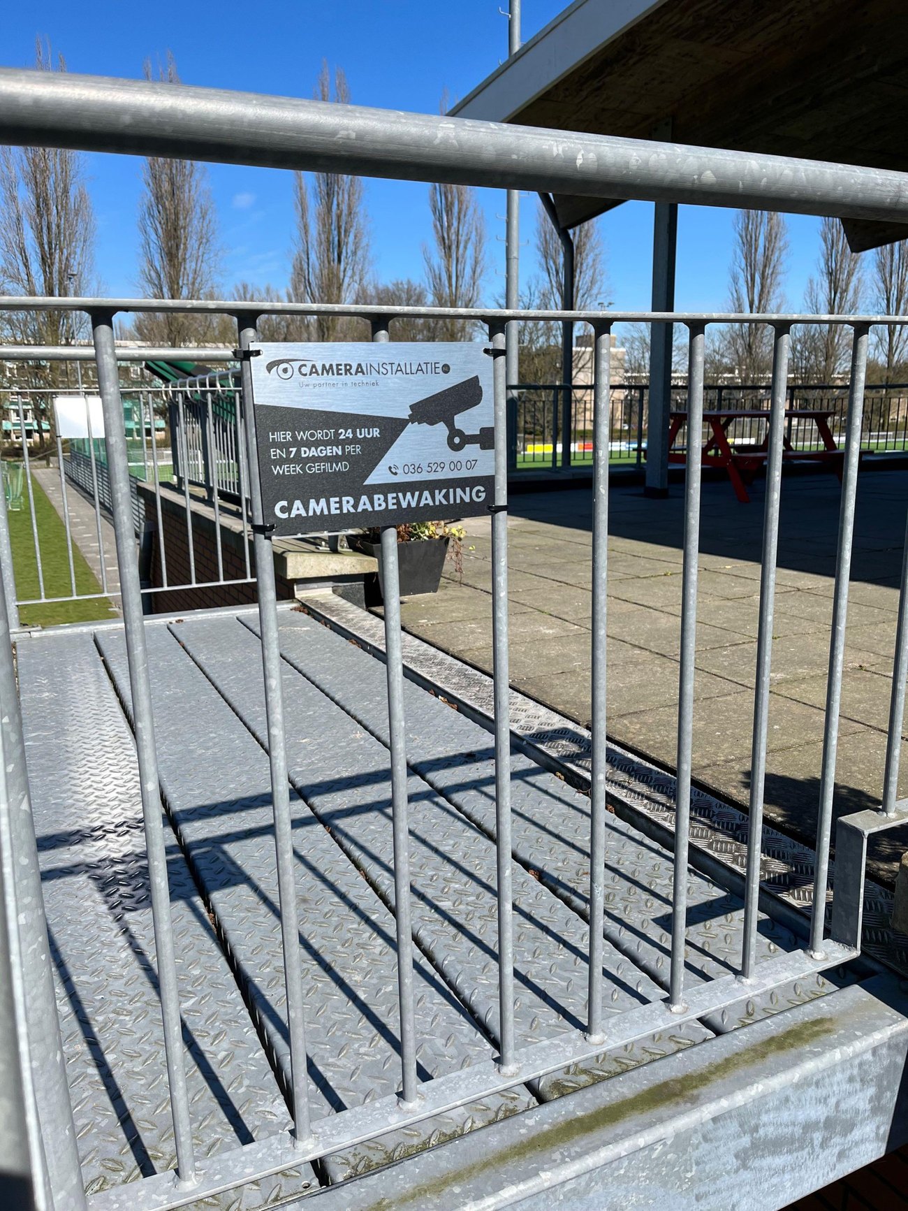 Bord met de tekst camerabewaking, hier wordt 24 uur en 7 dagen per week gefilmd, bevestigd aan een stalen hek