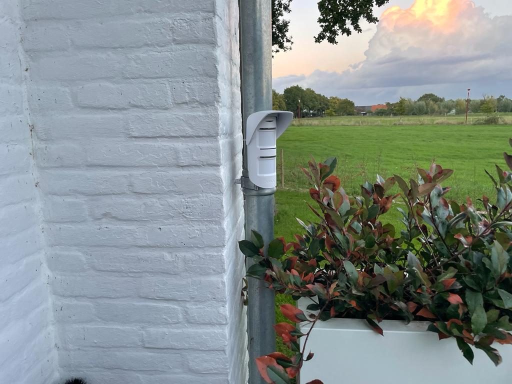 Buitendetector aan een witte gevel, gericht op de tuin