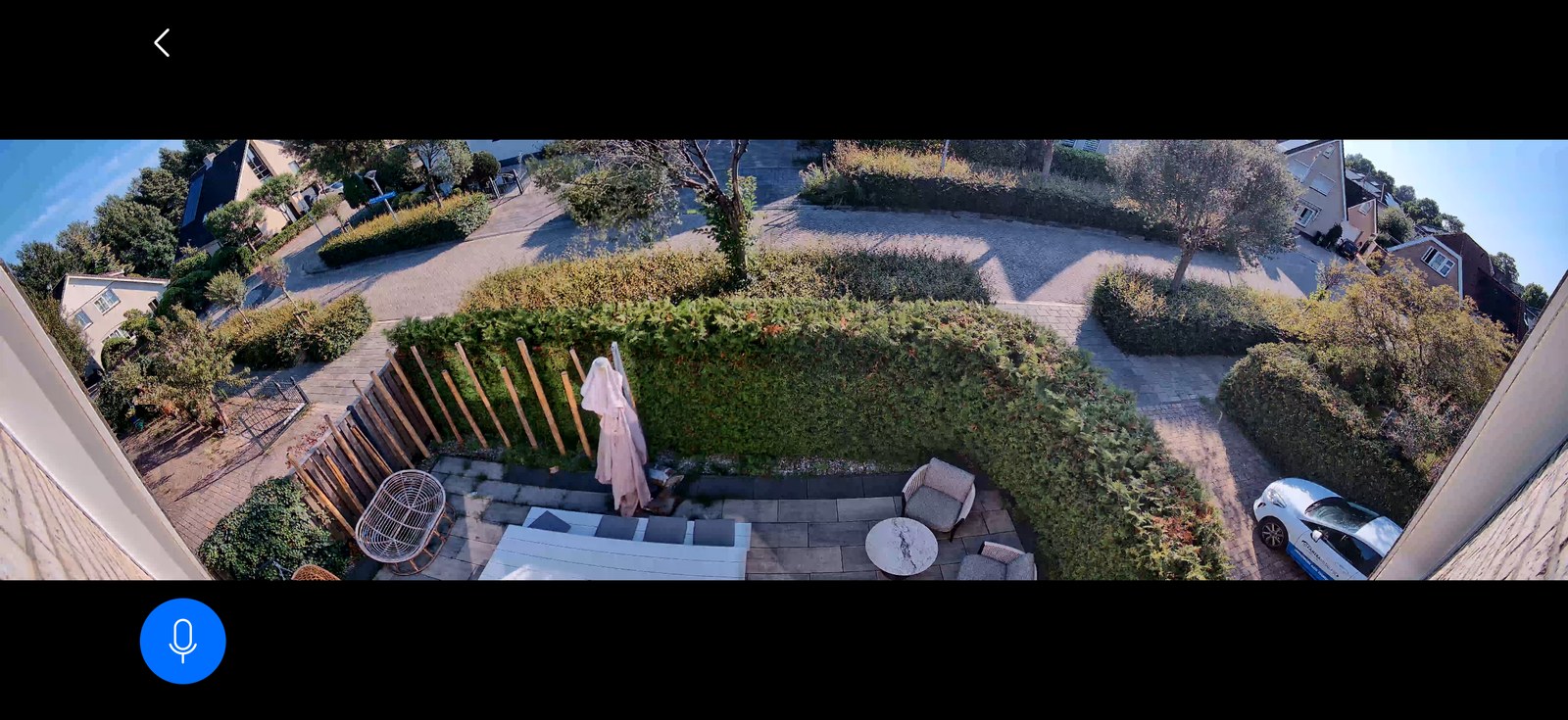 Panoramisch camerabeeld van bijna 180 graden over een tuin met terras, hagen en oprit — alles zichtbaar, maar klein