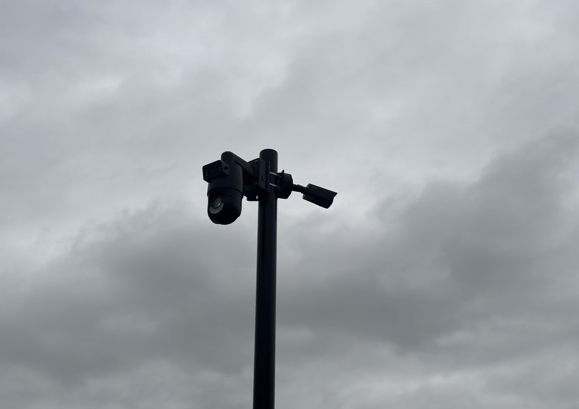Zwarte cameramast met een draaibare camera en een vaste camera tegen een donkere wolkenlucht