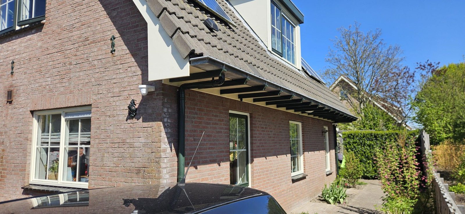 Witte camera onder de dakrand van een baksteenwoning, met zicht op het pad langs de zijgevel