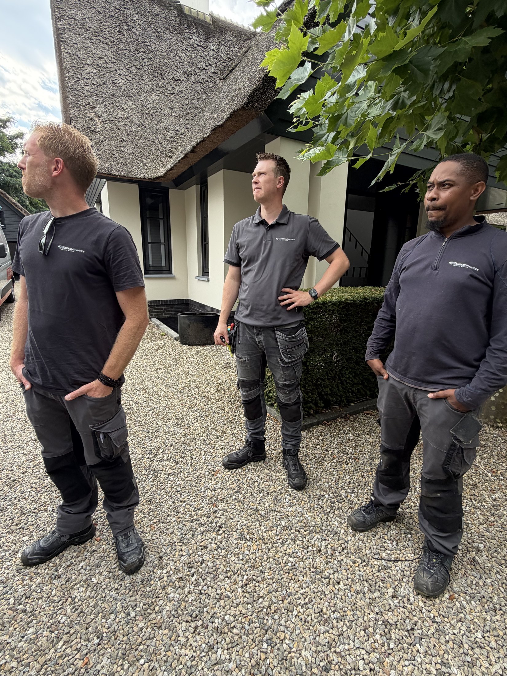 Drie monteurs in werkkleding op de oprit voor een rietgedekte villa