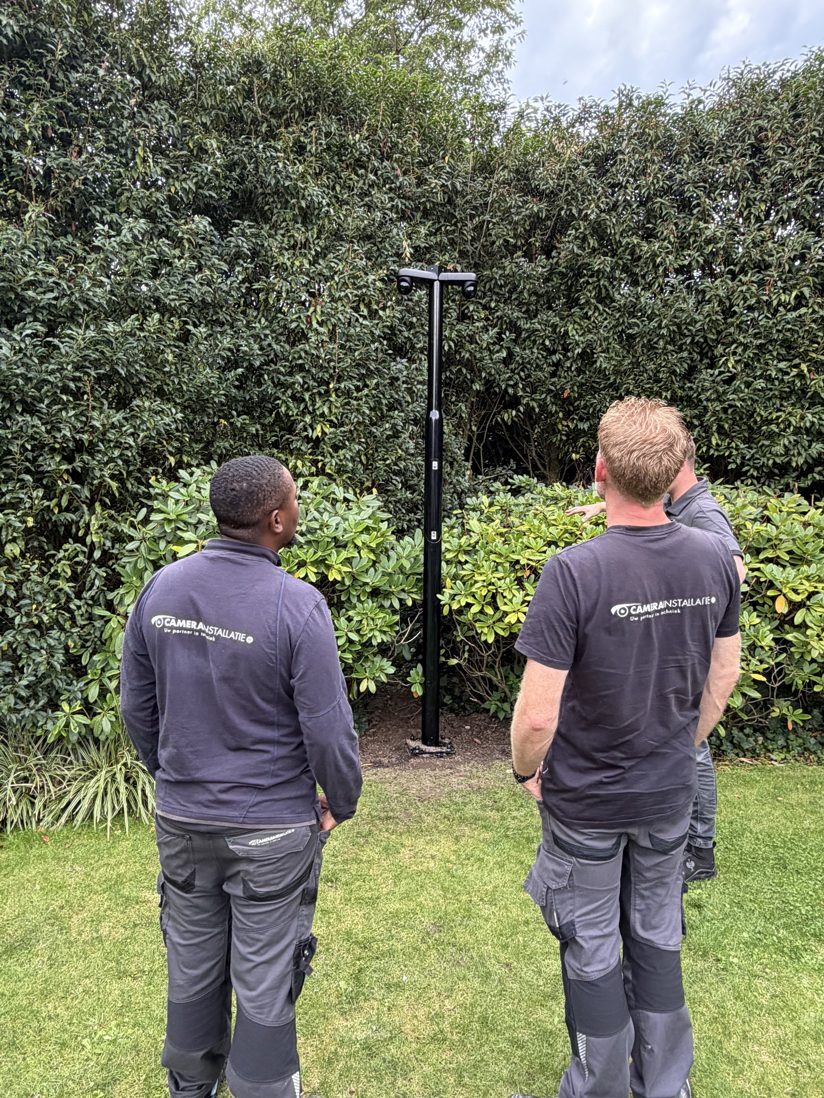 Twee monteurs bij een pas geplaatste zwarte camerapaal in een tuin
