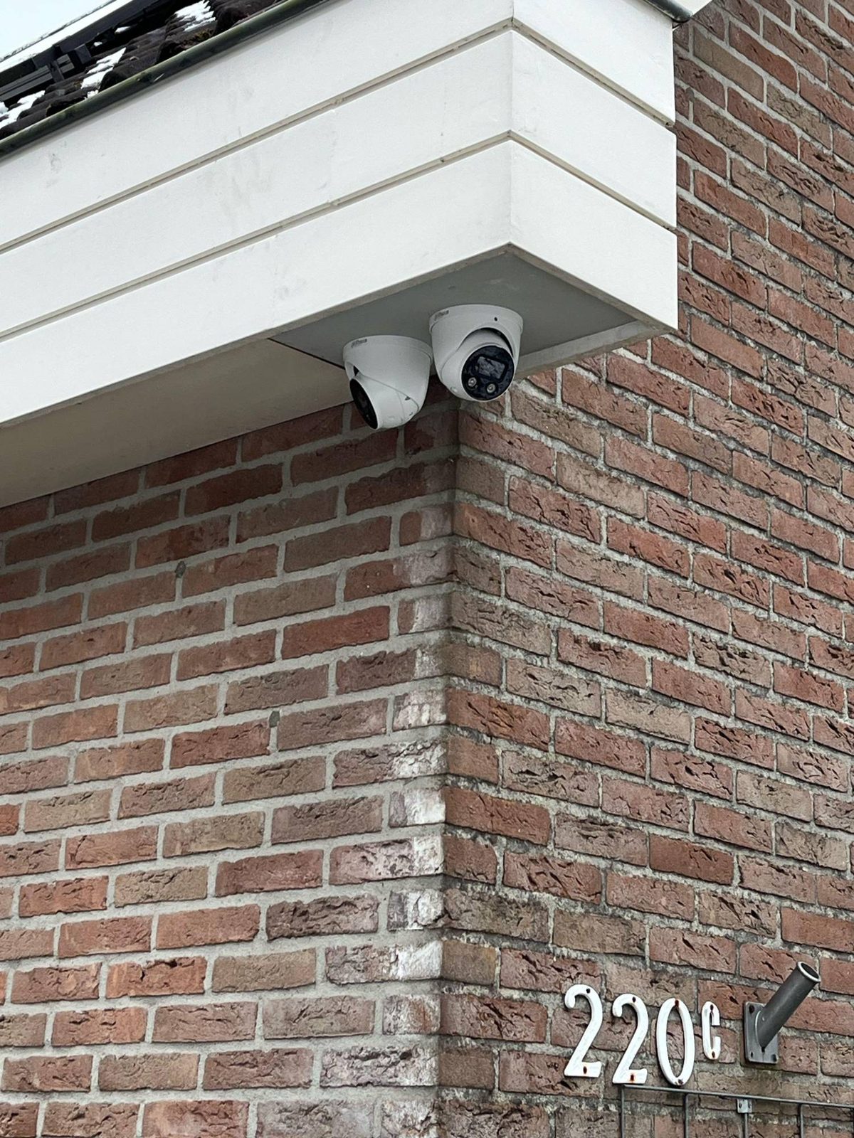 Twee witte camera's onder het witte boeideel op de hoek van een gemetselde gevel, elk een andere kant op gericht