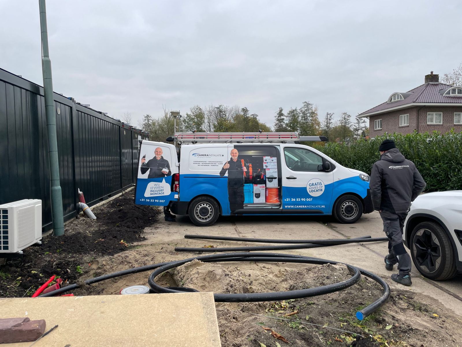 Zwarte mantelbuizen liggen klaar op een terrein met units, onze bus met open deuren ernaast