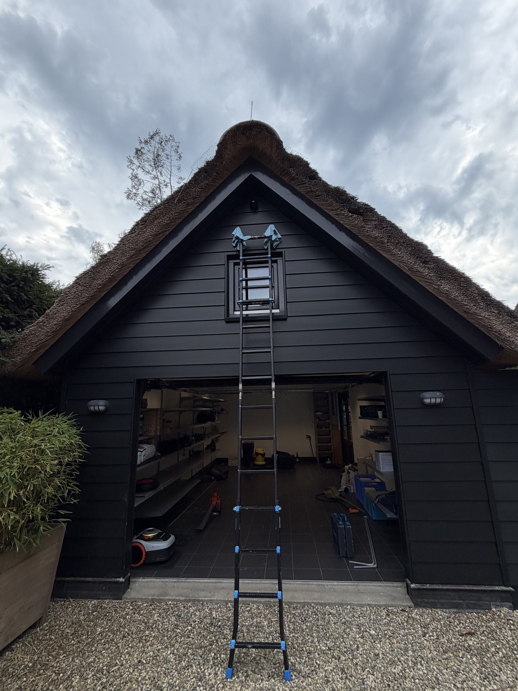 Ladder tegen de gevel van een donker rietgedekt bijgebouw met open garagedeur
