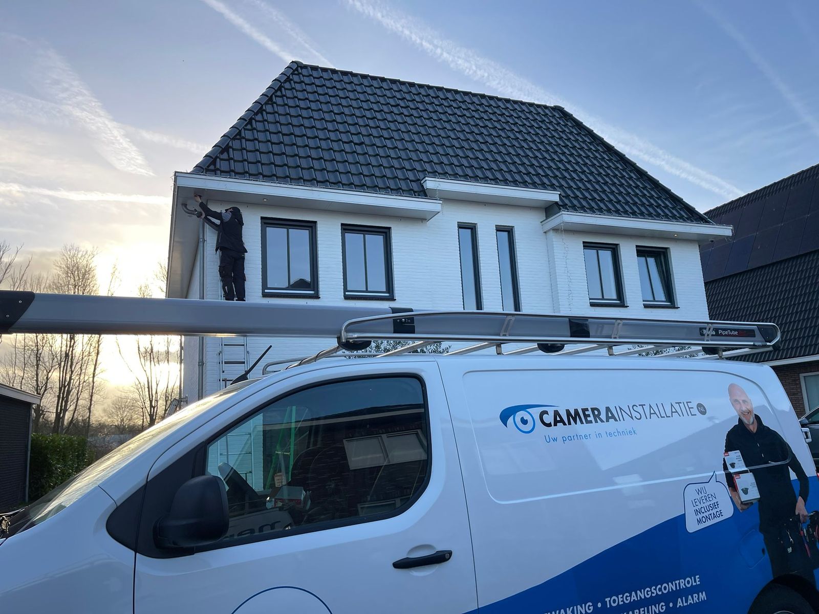Monteur op de ladder werkt aan een camera aan de zijgevel van een woning