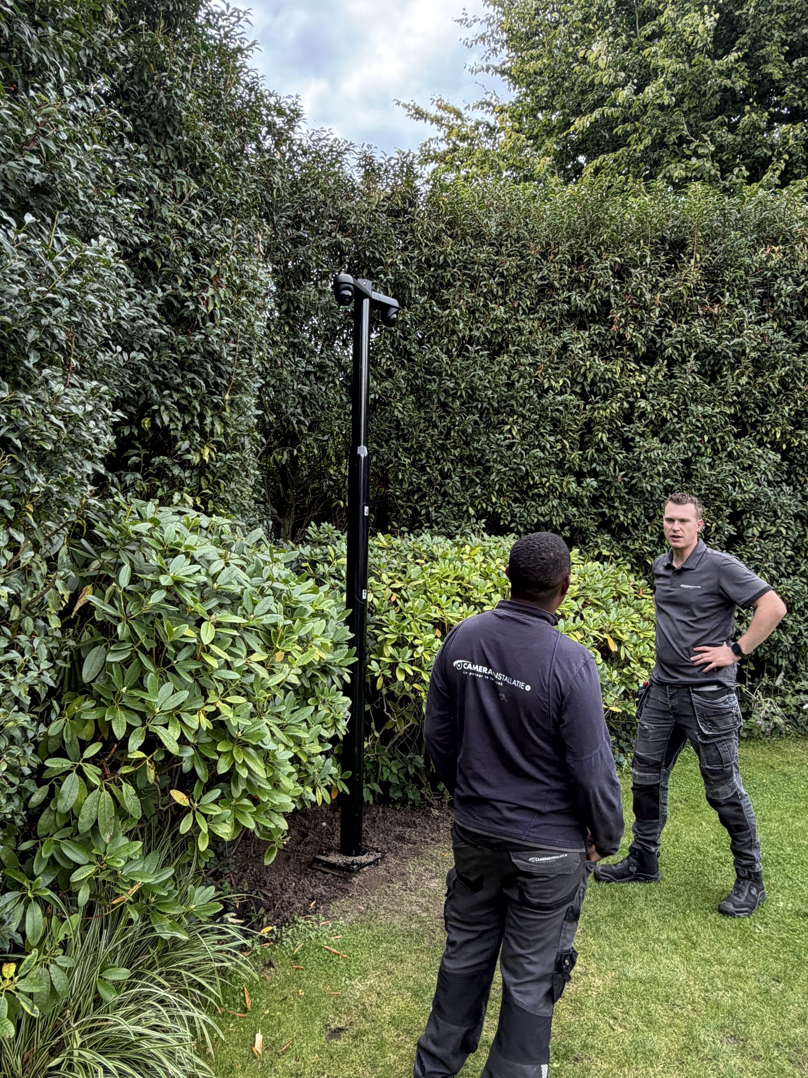 Monteur bij een camerapaal terwijl een collega op afstand meekijkt