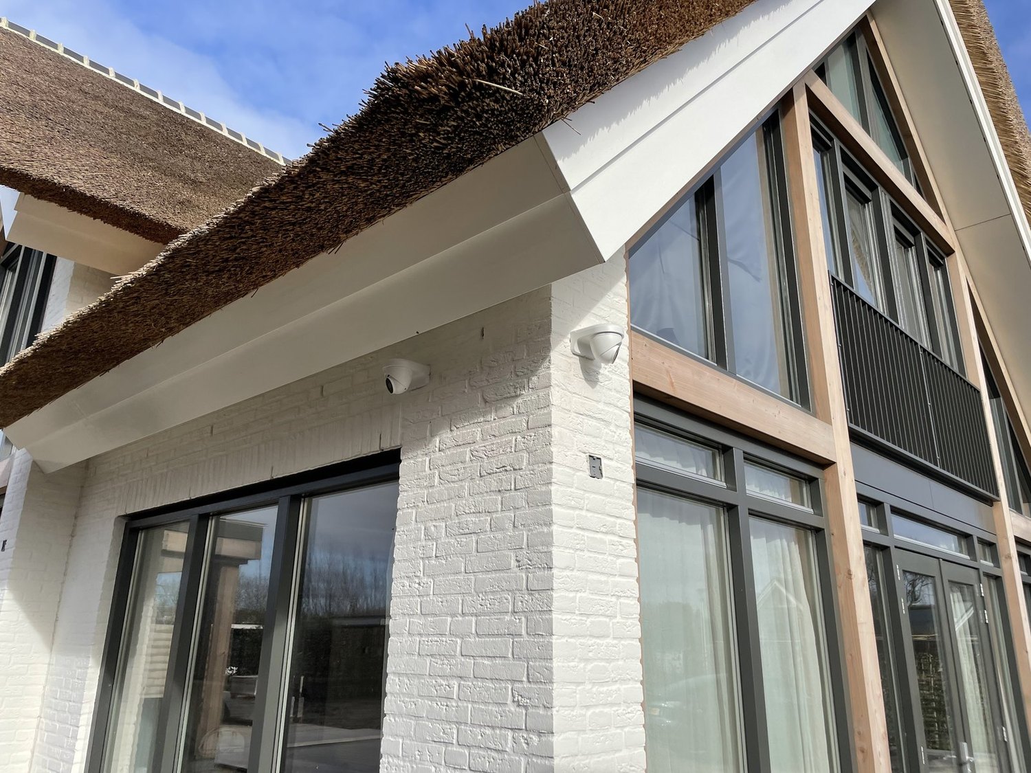 Wit landhuis met rieten kap: witte camera onder het overstek en een tweede camera op de hoek boven de pui