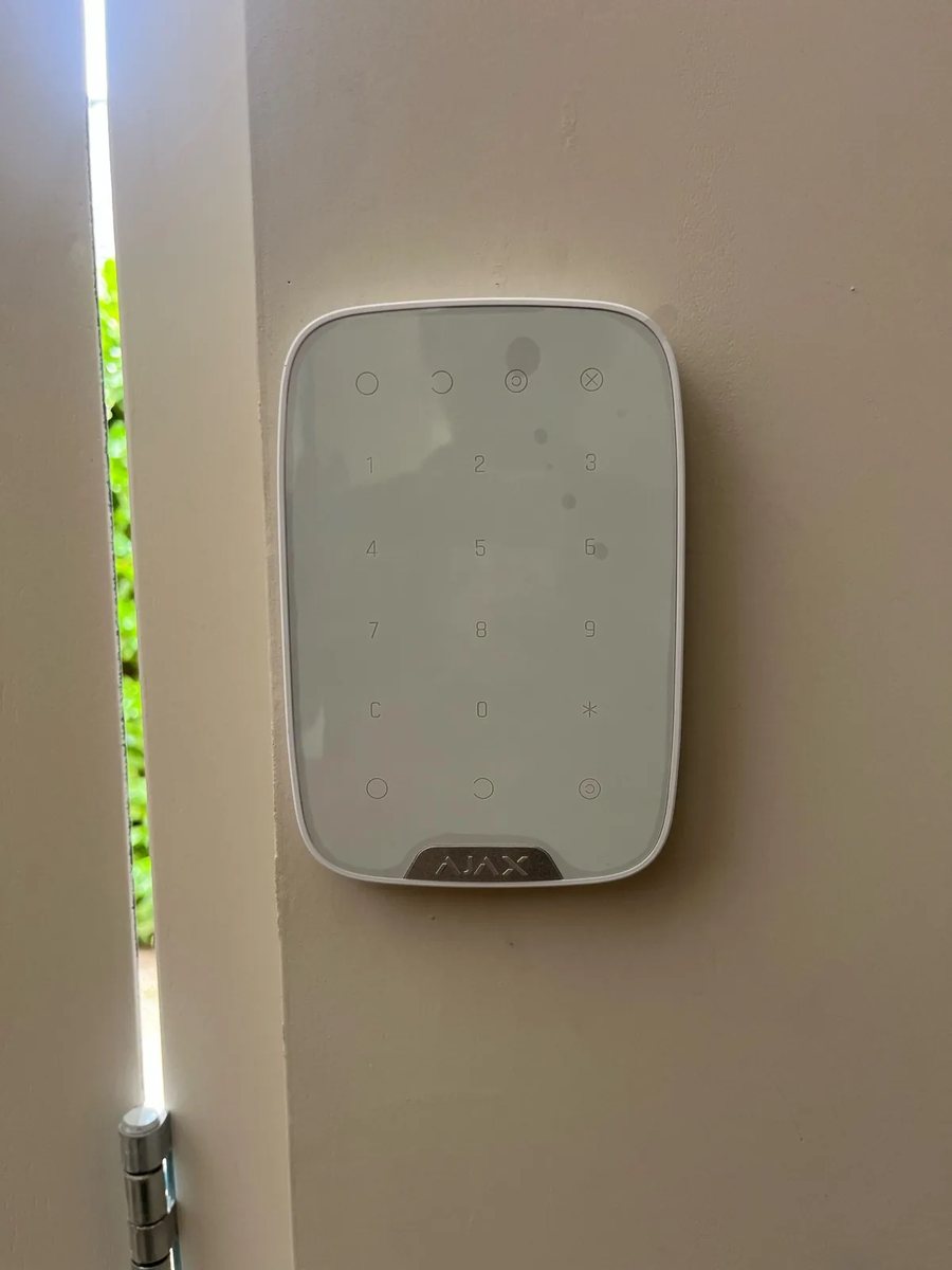 Wit Ajax-bediendeel met cijfertoetsen aan een lichte wand naast een deur