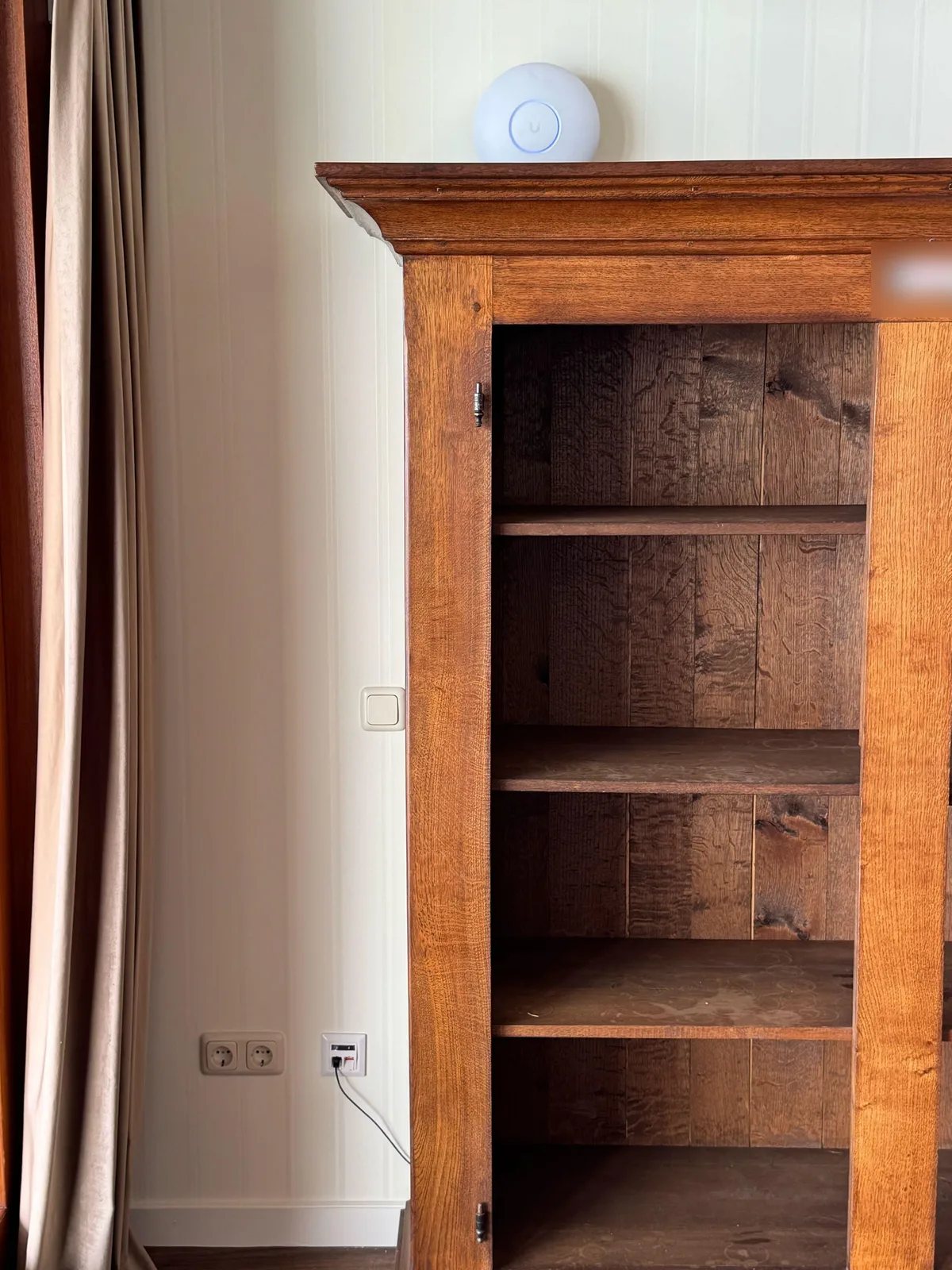 Wit rond access point bovenop een eikenhouten kast, met een netwerkaansluiting in de muur ernaast