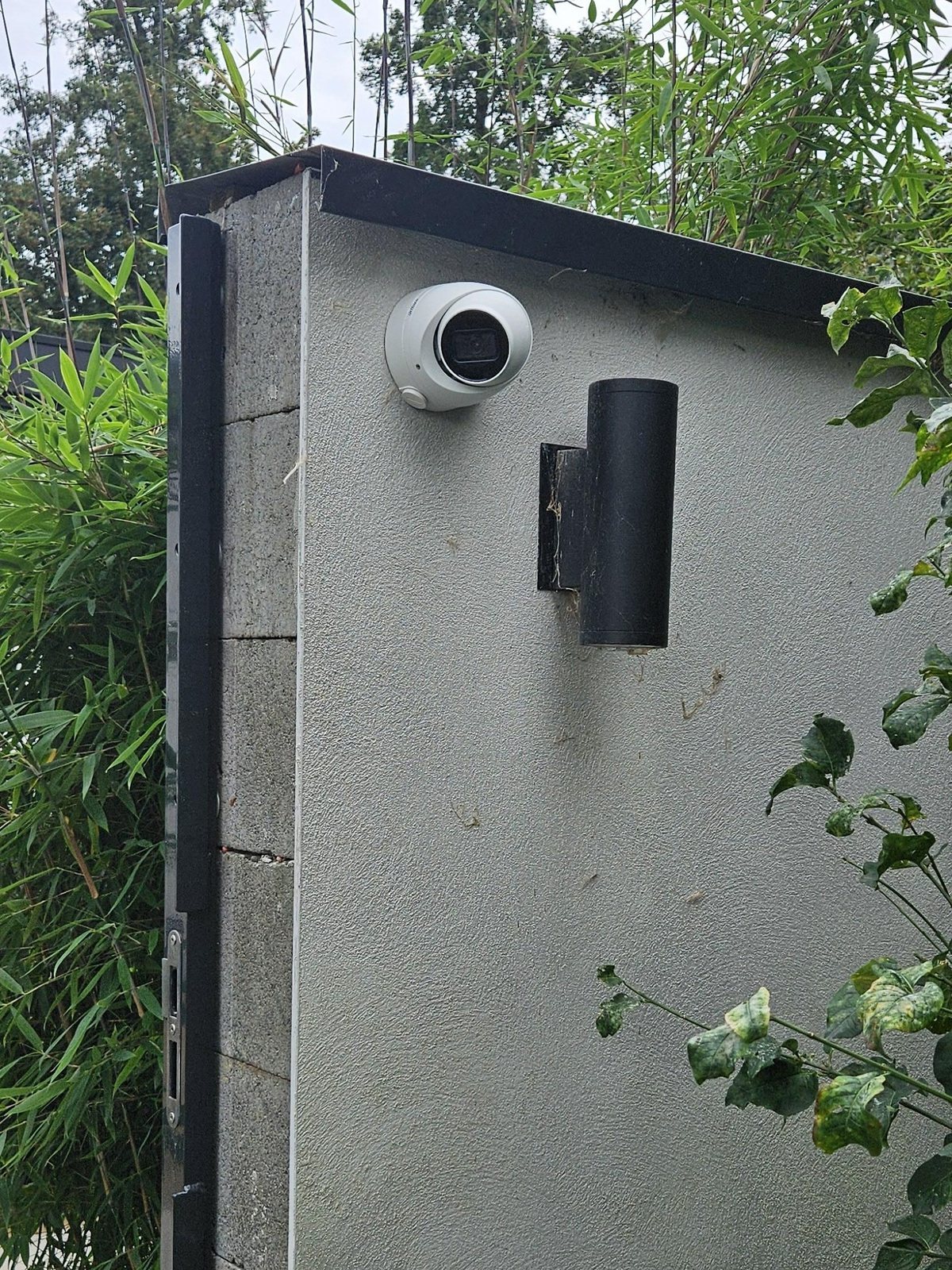 Camera op een muur naast een poort, met bamboe erachter