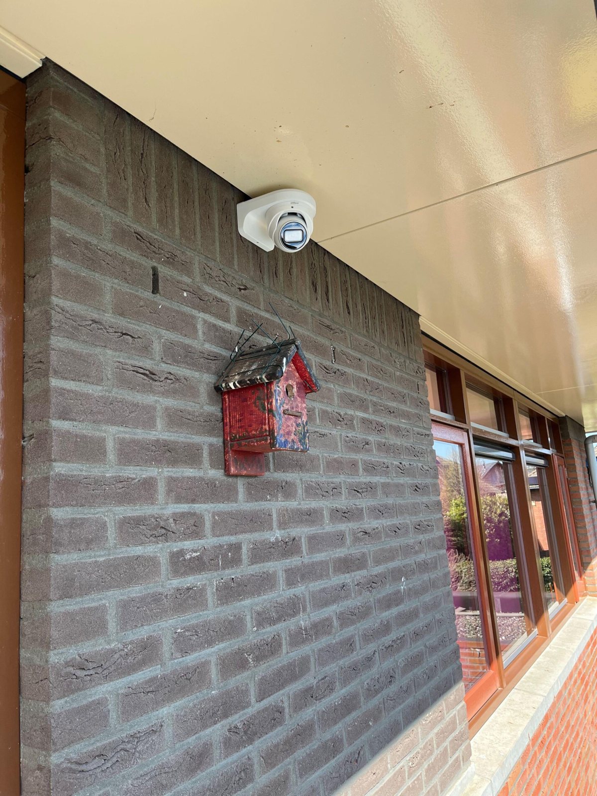 Witte camera hoog op een grijze bakstenen muur bij een zijpoort onder een overkapping