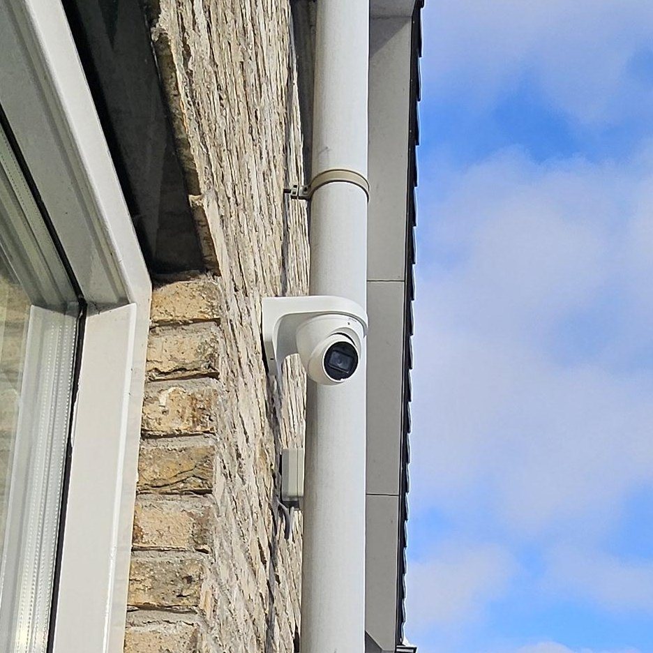 Witte camera hoog op een gevel, vlak naast een regenpijp