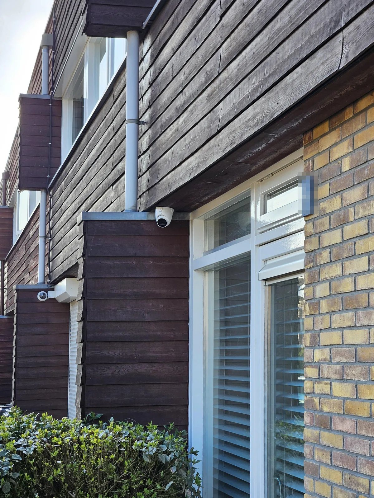 Witte camera op een erker onder een houten overstek van een rijwoning, zonder zichtbare kabel