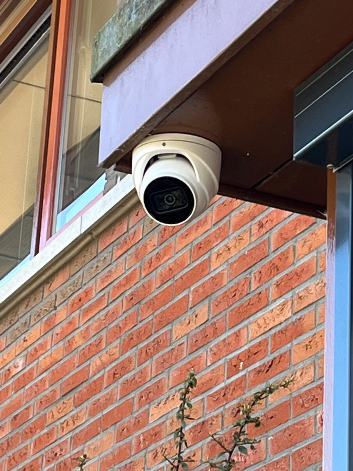 Witte turretcamera onder een donker overstek, boven een rode bakstenen muur