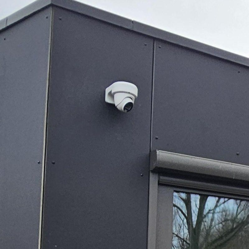 Zwarte dome-camera op een donkere gevel, onder de dakrand