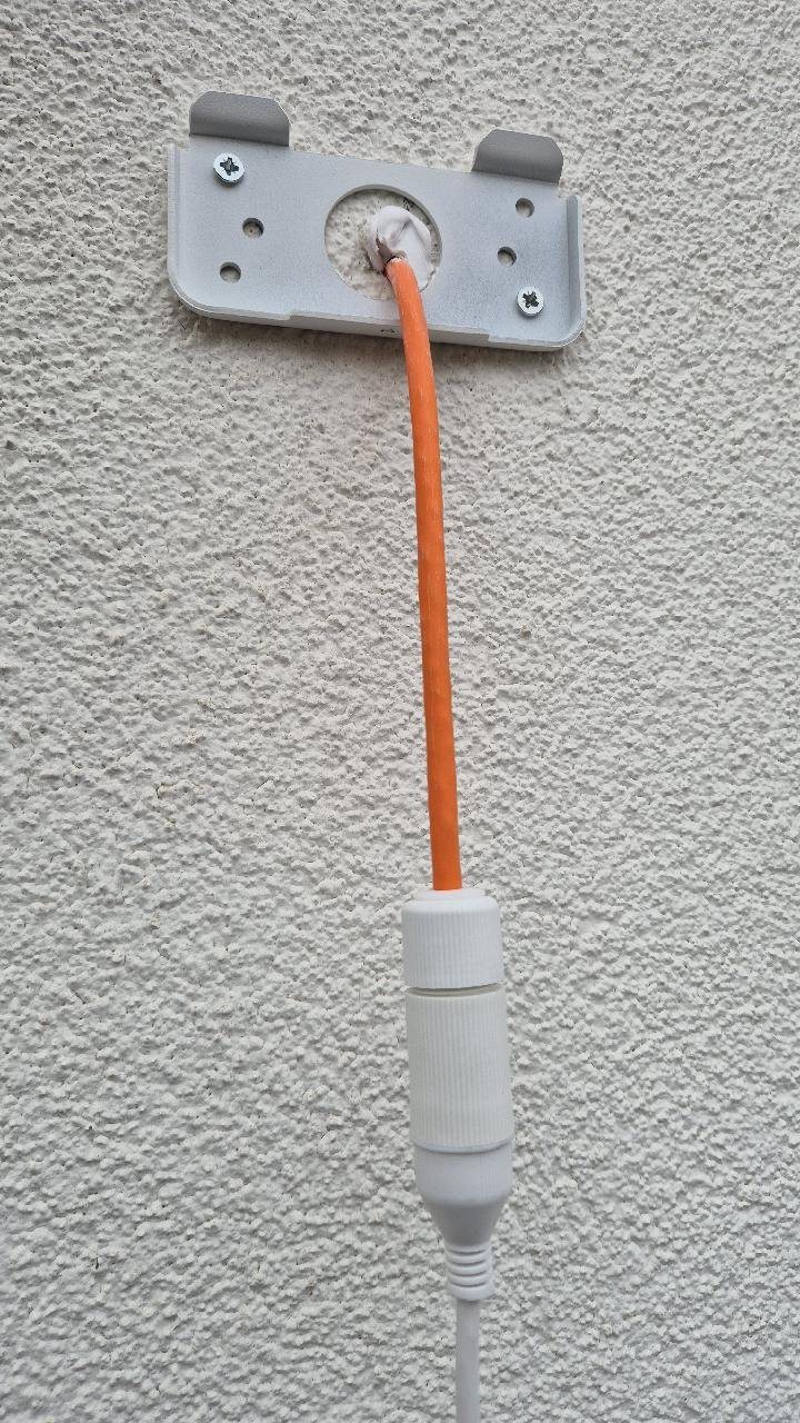 Kabel in een witte flexbuis die strak langs een lichte gevel omhoog loopt