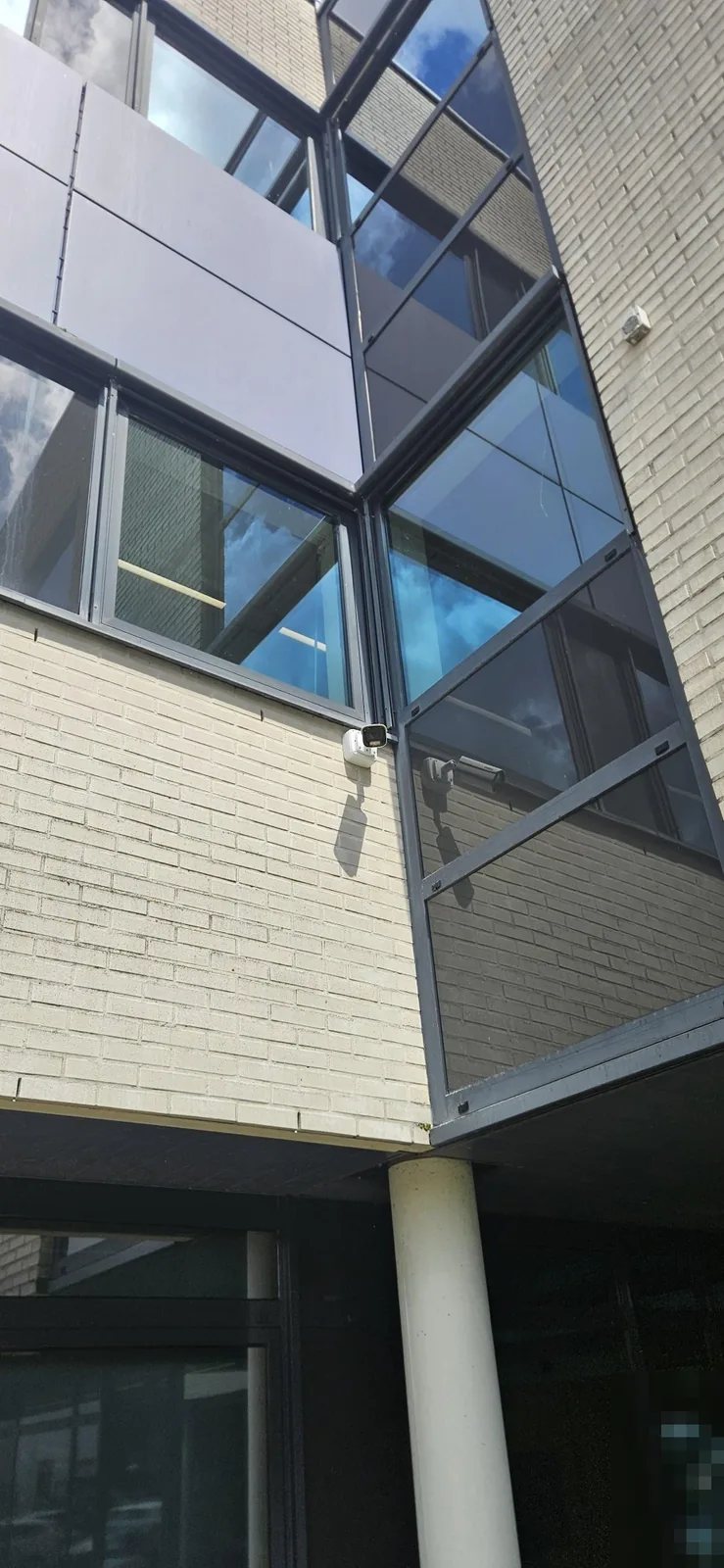 Witte camera op de gevel van lichte baksteen, naast een glazen trappenhuis