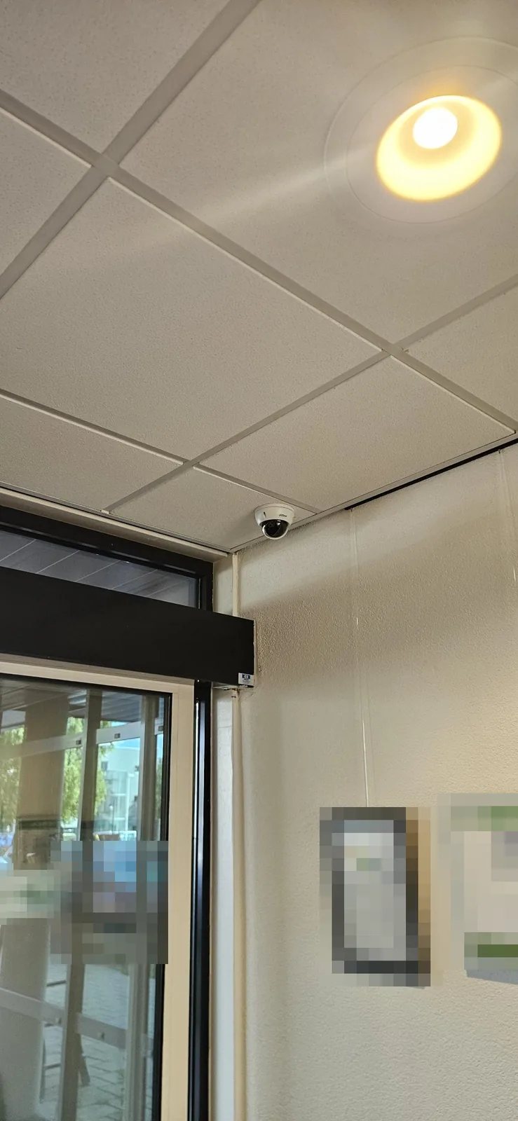 Witte domecamera in de hoek van een systeemplafond boven een schuifdeur in de hal