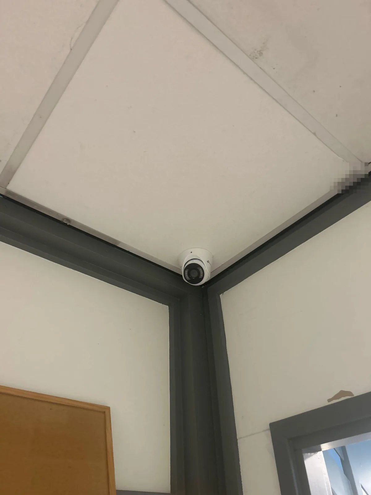 Witte turretcamera in de hoek van een wit systeemplafond boven grijze kozijnen