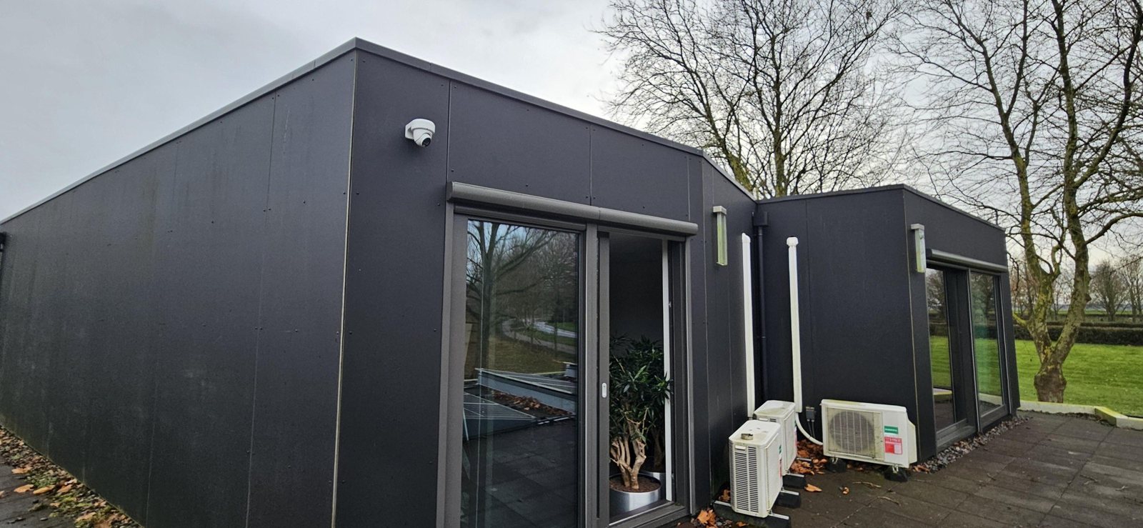 Moderne woning met donkere gevels en grote ramen, met een camera onder de dakrand