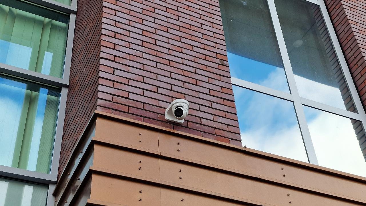 Camera op een steun tegen een bakstenen gevel naast grote ramen