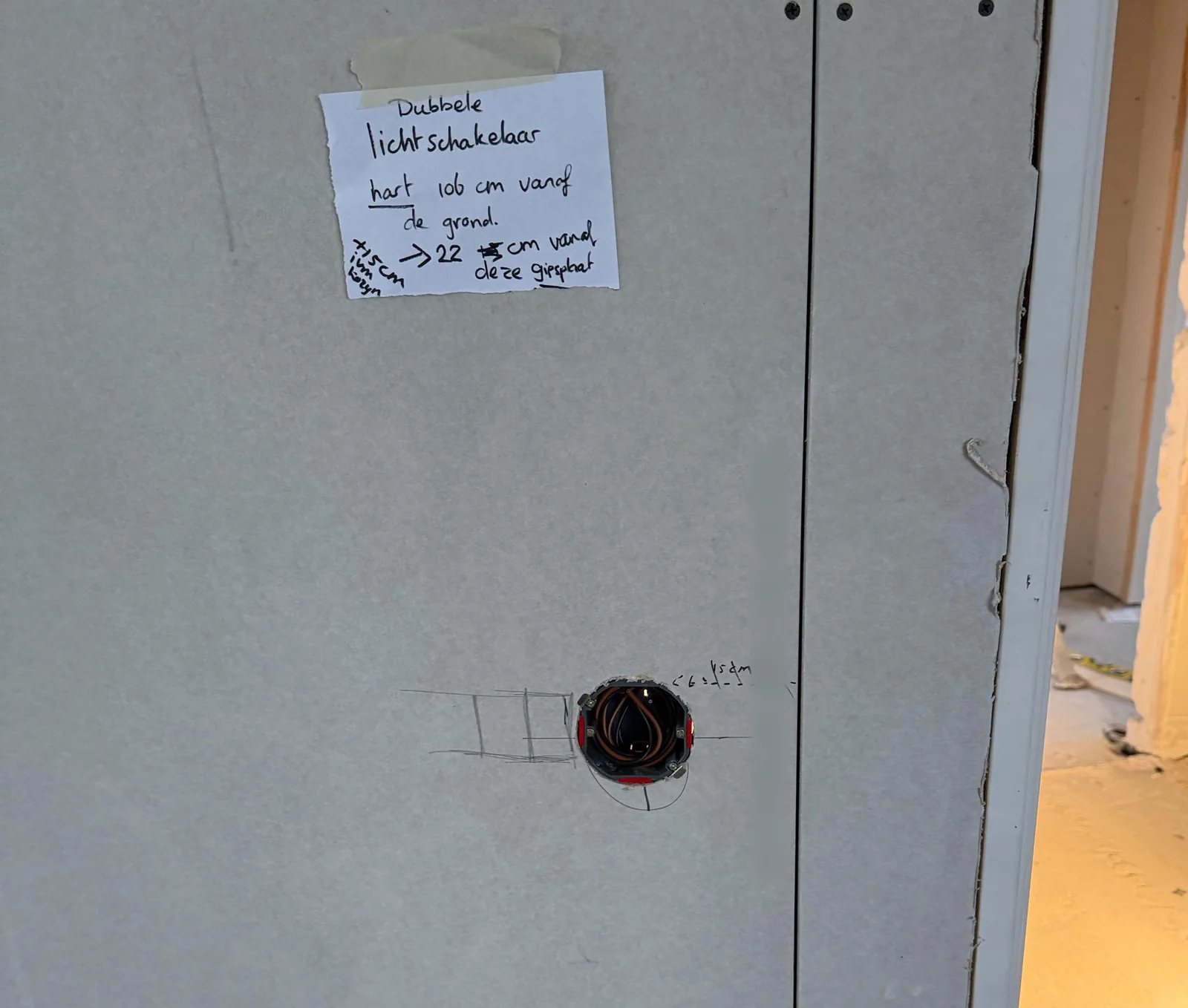 Handgeschreven briefje op een gipsplaat over een dubbele lichtschakelaar op 106 centimeter, met eronder een hollewanddoos