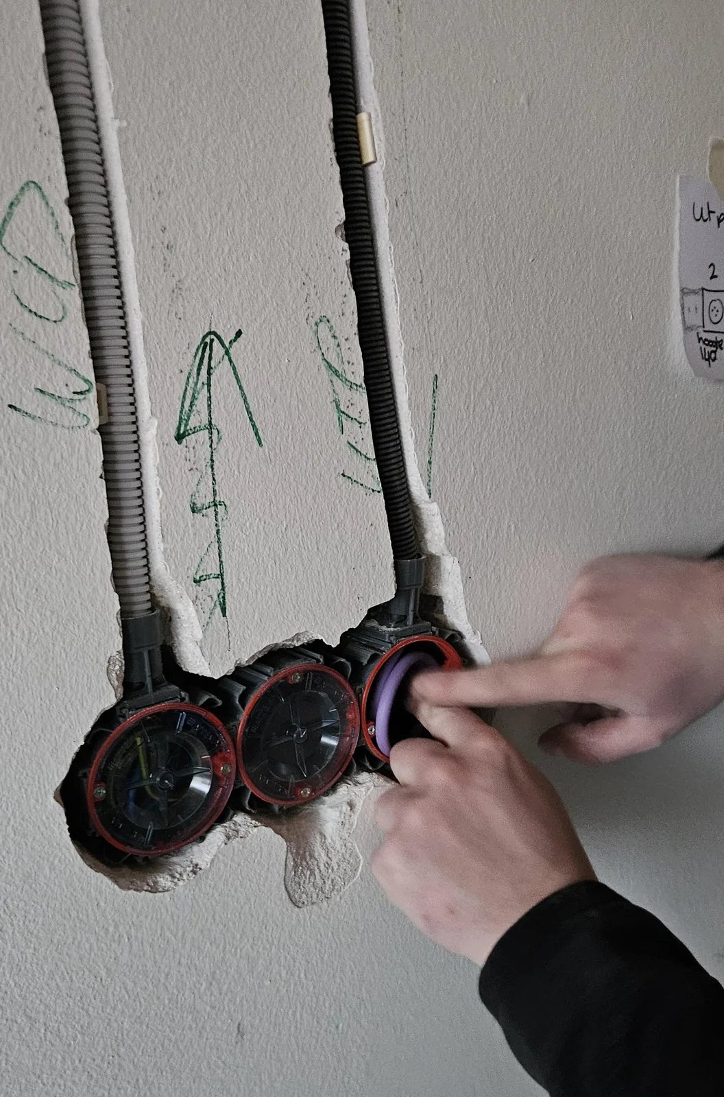 Twee handen duwen een paarse netwerkkabel in een inbouwdoos, met UTP en WCD in groene verf op de muur