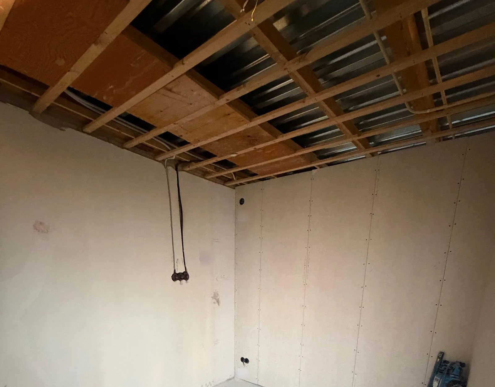 Kamer in verbouwing met een open plafond van houten regels en staalplaat, en buizen langs de wand naar inbouwdozen