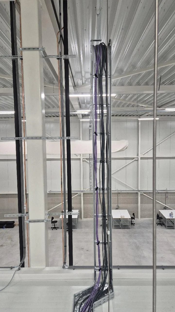 Bundel paarse en zwarte kabels die verticaal langs een kolom naar boven loopt in een lege warehousehal