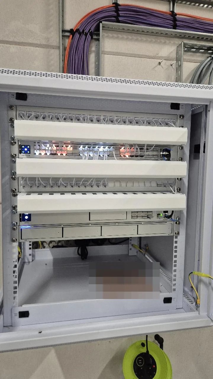 Witte patchkast met patchpanelen, een switch met verlichte poorten en router, en paarse kabelbundels in de goot erboven