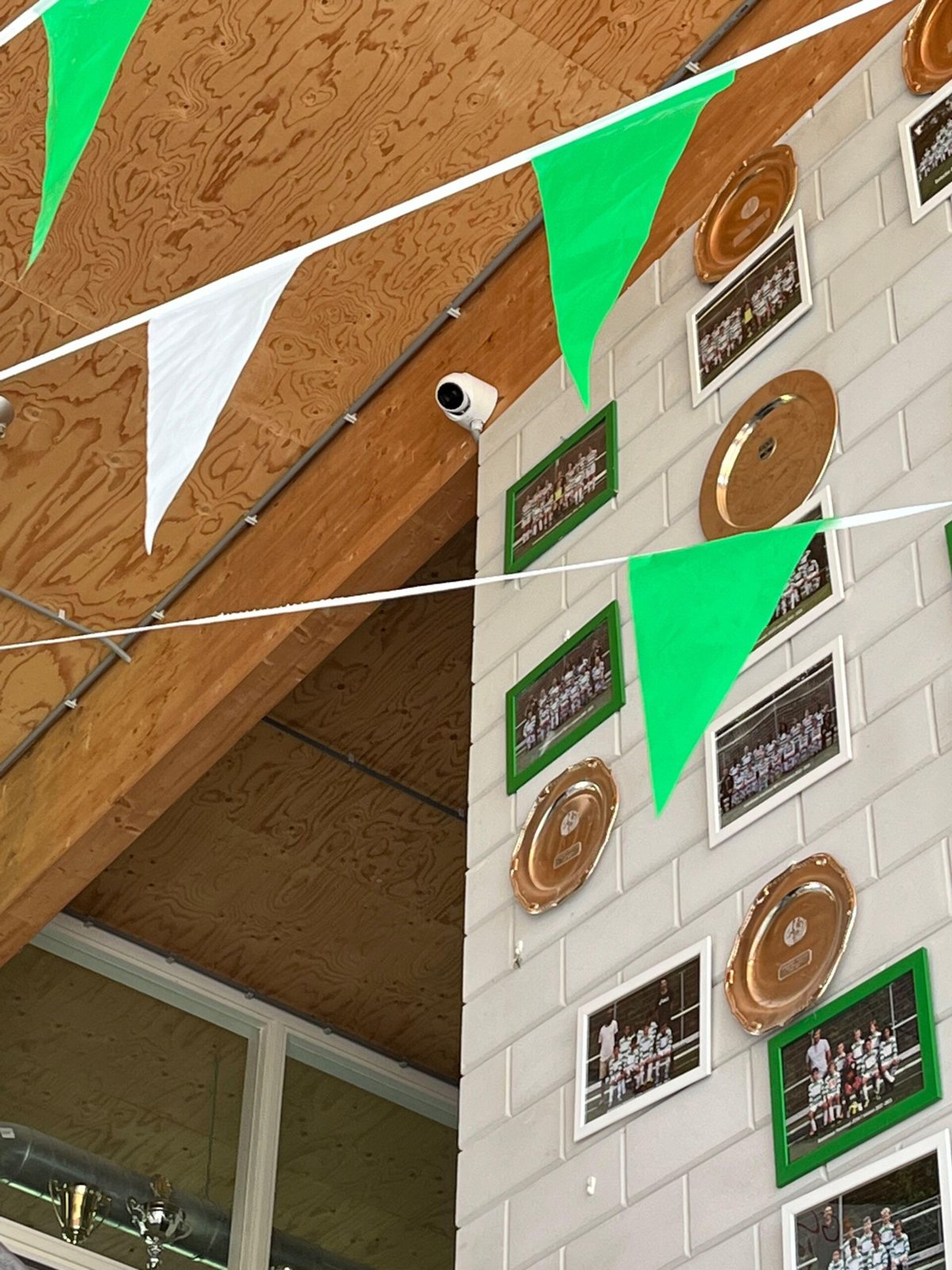 Camera hoog in de kantine tussen teamfoto's en schalen aan de wand
