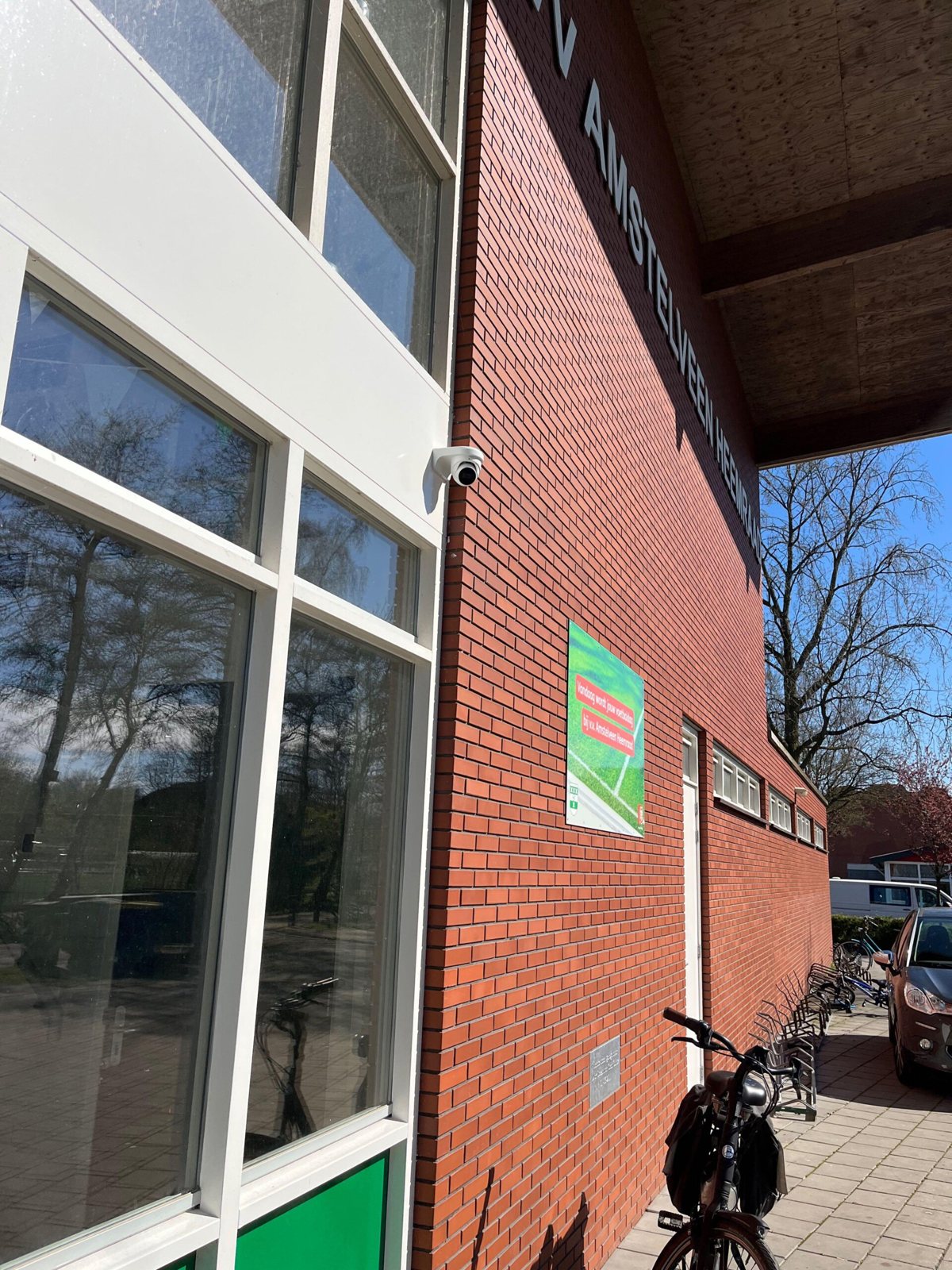 Camera aan de gevel van een clubhuis, met zicht op de fietsenrekken
