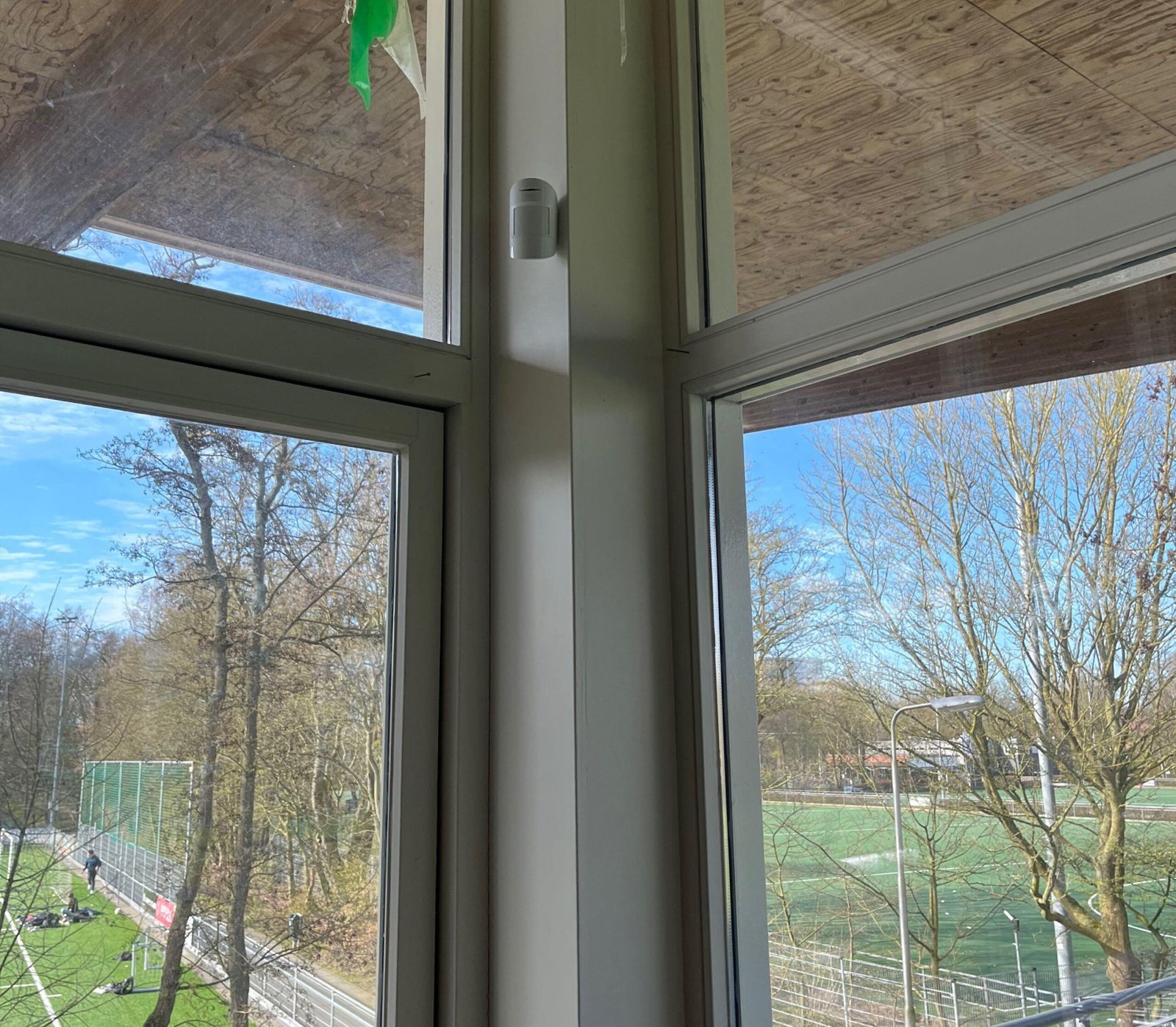 Uitzicht vanuit het clubhuis op het voetbalveld, met een melder op de raamstijl