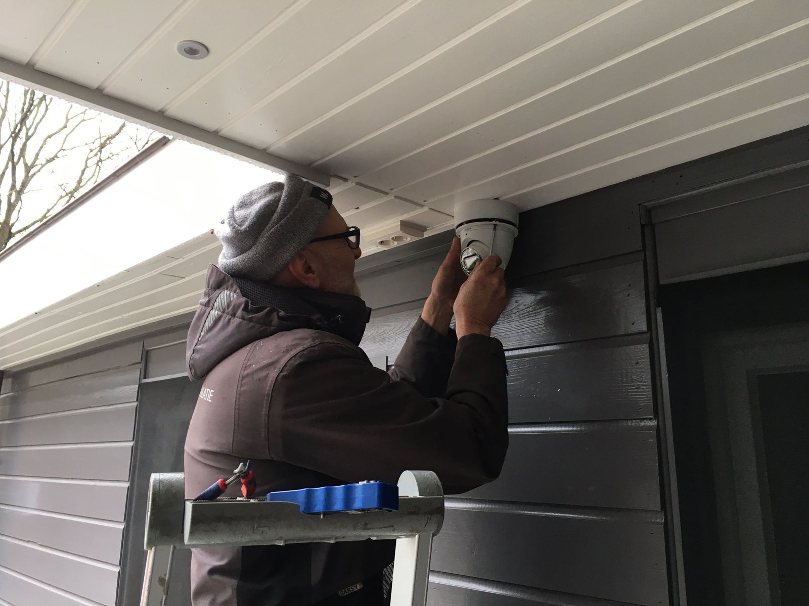 Monteur op een trap monteert een witte domecamera onder de dakrand van een chalet
