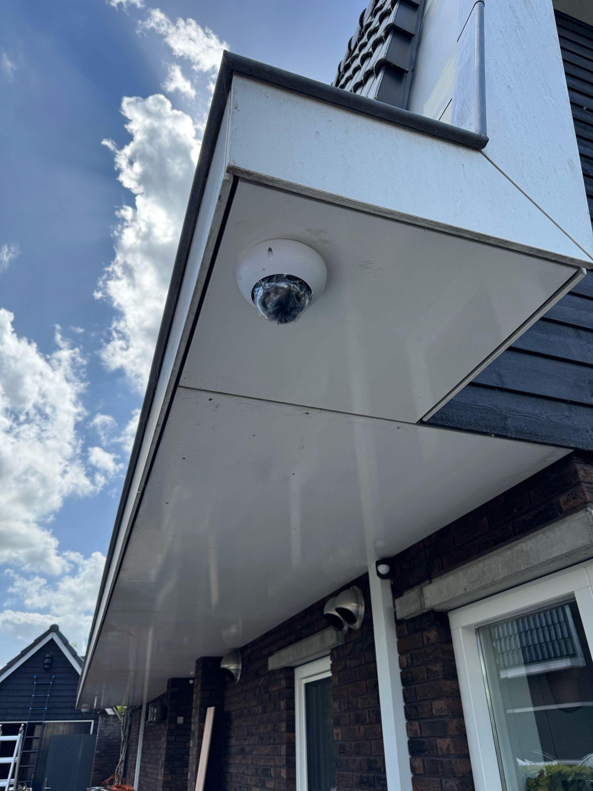 Witte dome-camera onder een wit overstek, tegen een blauwe lucht