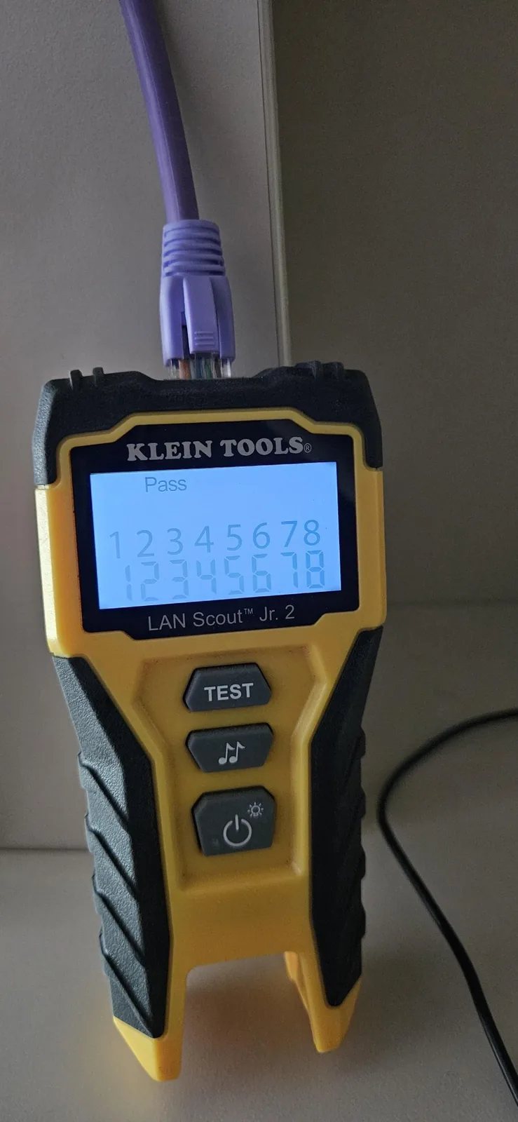 Gele kabeltester met op het scherm Pass en alle acht aders van een paarse netwerkkabel