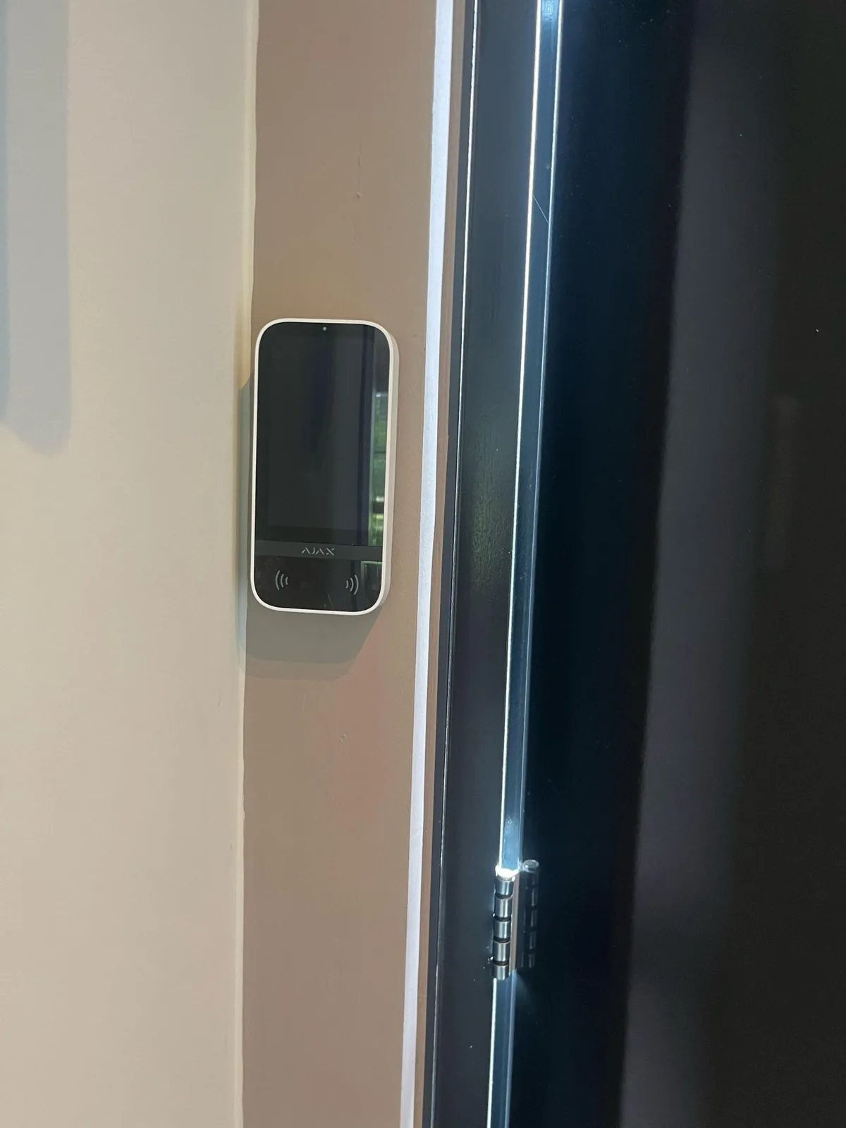 Wit Ajax-bediendeel met touchscreen op een lichte wand naast een zwarte deur