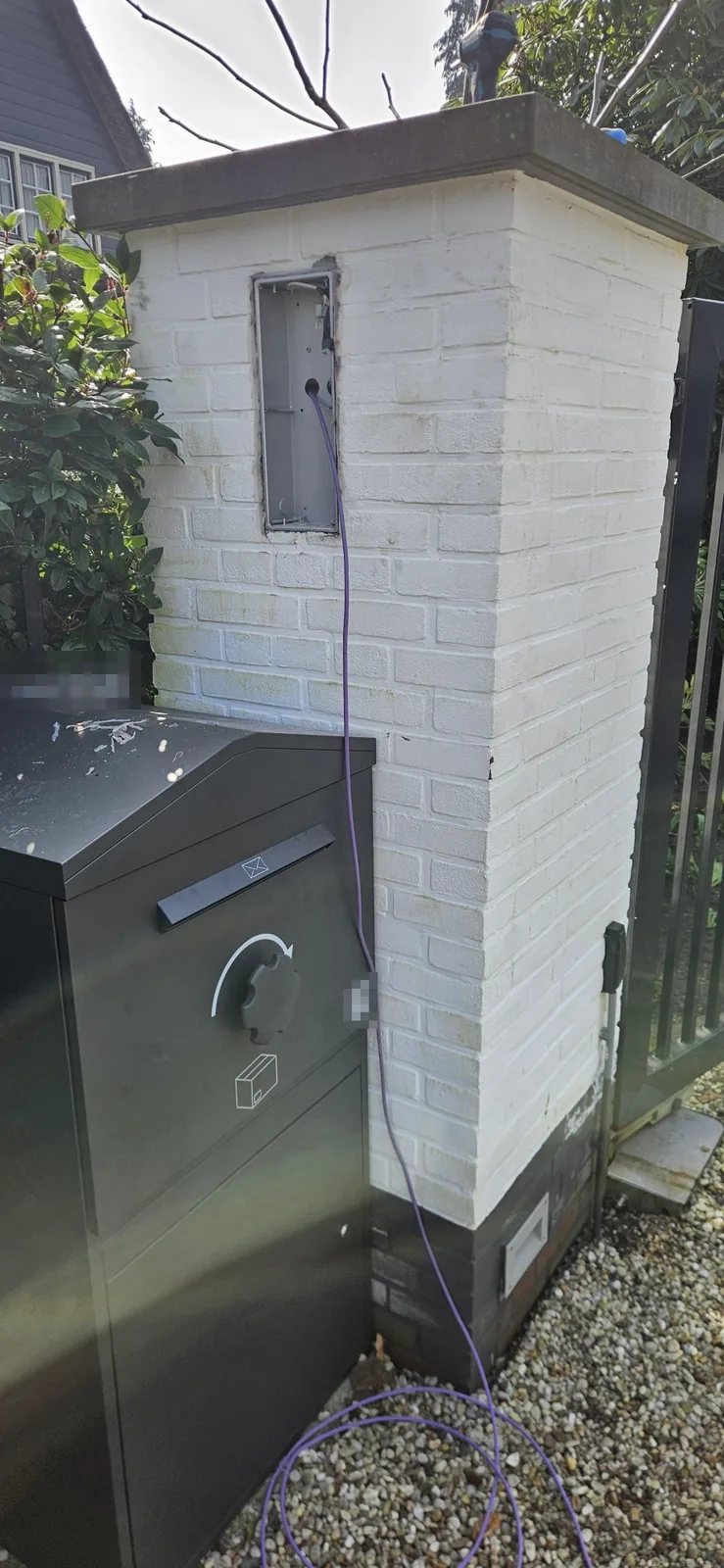 Witte gemetselde pilaar bij een poort met een lege inbouwdoos en een paarse netwerkkabel die eruit hangt