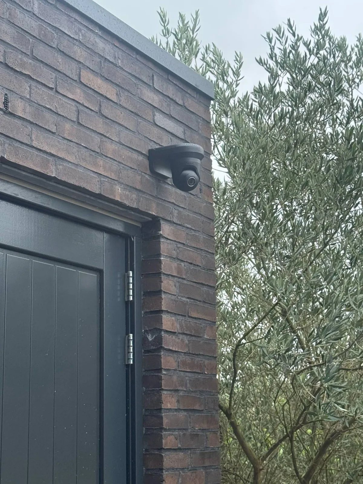 Zwarte camera op een zwarte beugel tegen donkere baksteen, boven een antraciet deur