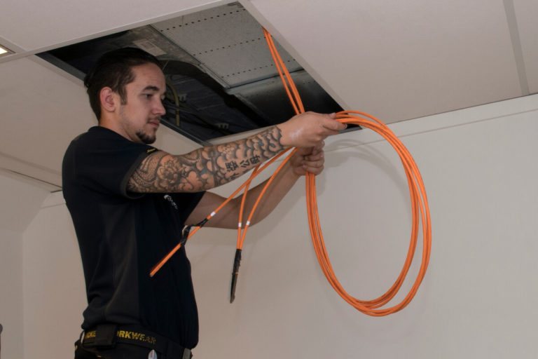 Monteur trekt een oranje kabel uit een open plafondluik