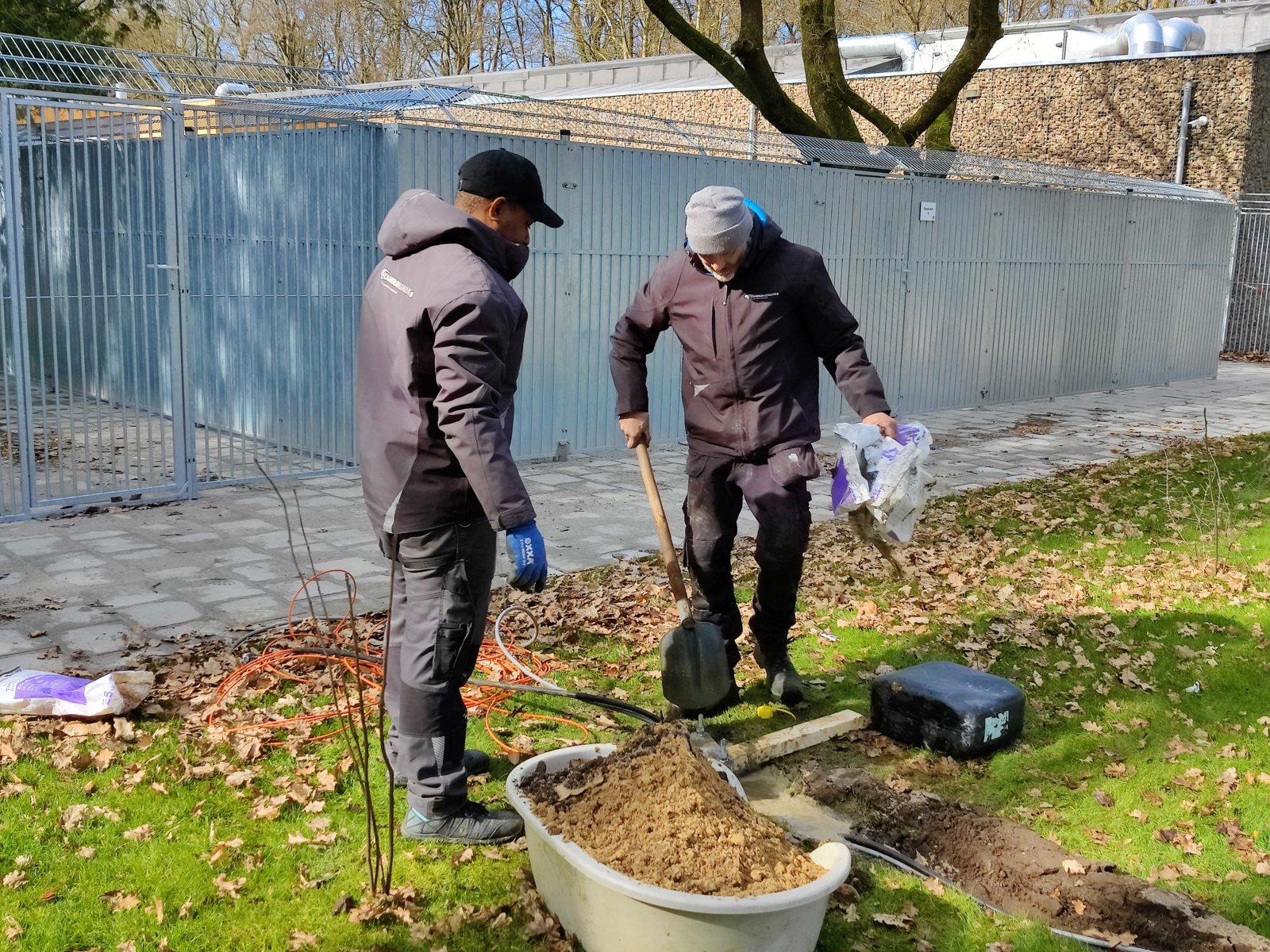 Twee monteurs graven een sleuf in het gras voor een kabel naar de weiden