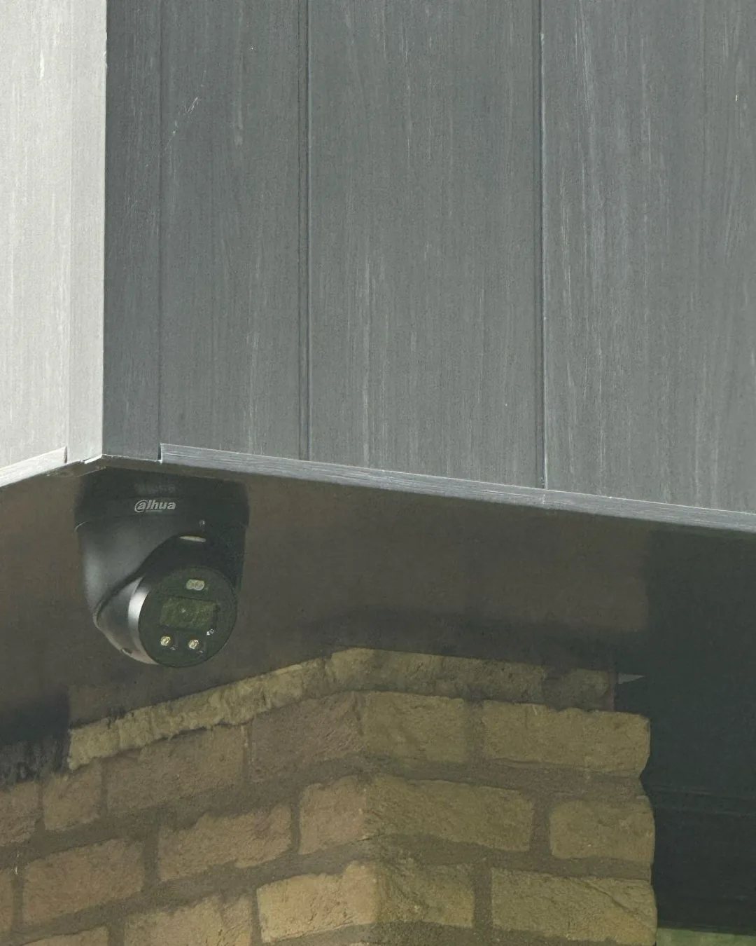 Zwarte Dahua-camera onder een donker overstek, vlak boven gele baksteen