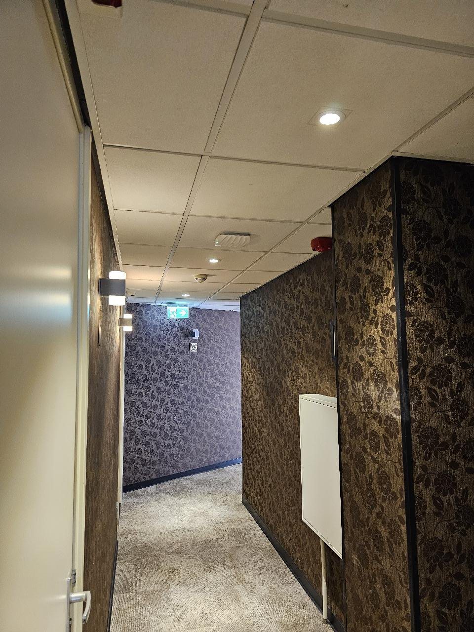 Hotelgang met donker behang en een witte wifizender aan het plafond