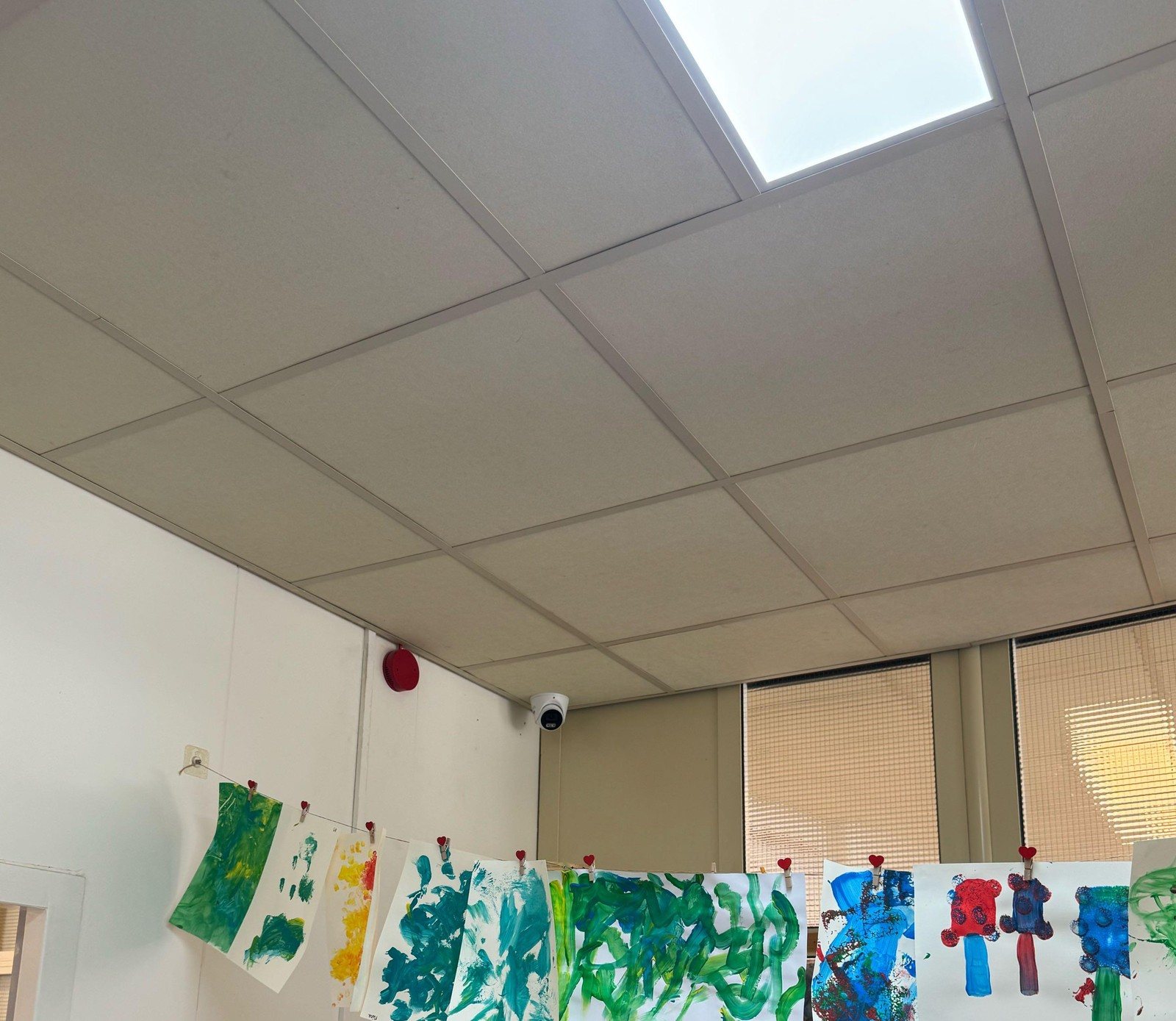 Witte camera in de hoek van een groepsruimte, met kindertekeningen aan een lijn