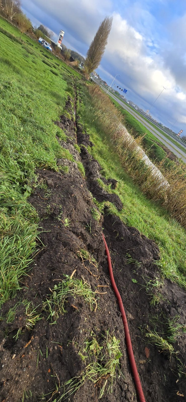 Smalle kabelsleuf langs een grasberm, met de kabel erin