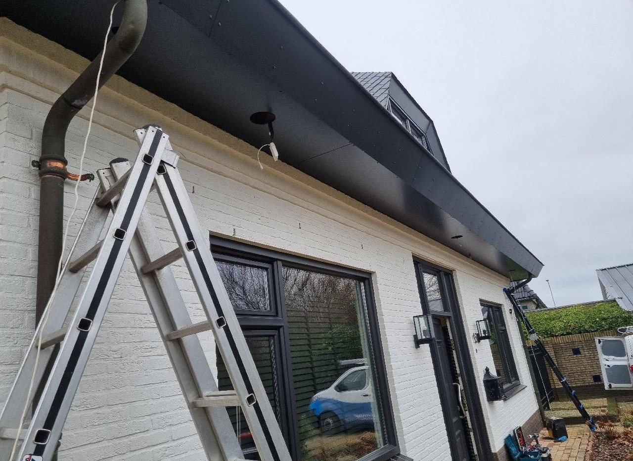 Witte woning met zwarte dakrand, een ladder tegen de gevel tijdens de montage