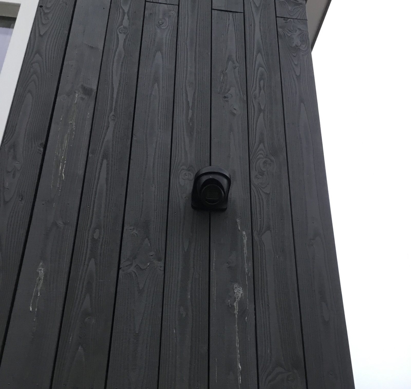 Kleine zwarte camera op een zwarte houten gevel, schuin van onderen gezien