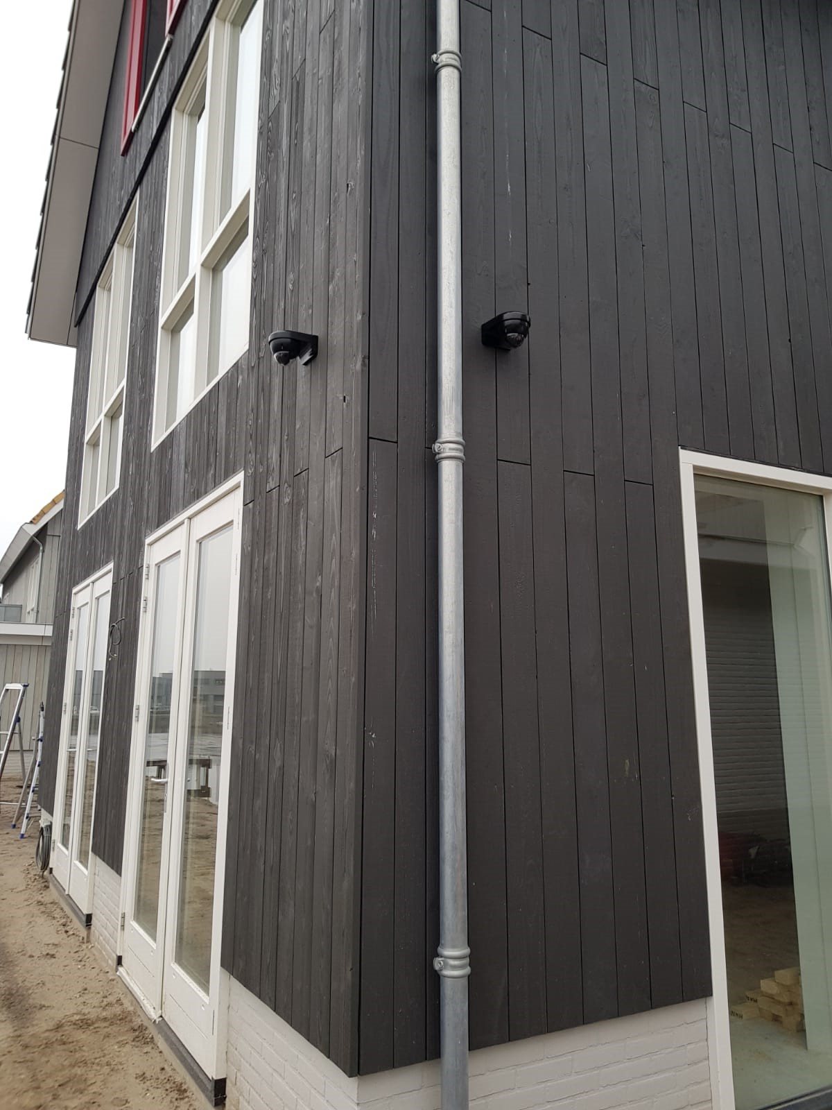 Donkere houten gevel van een woning met een kleine zwarte camera hoog aan de muur